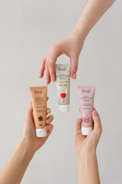 trzy ręce i każda z nich trzyma jeden krem, pierwszy to Hagi Krem do Rąk Regenerujący SOS Korzenna Pomarańcza 50ml - tubka drugi to Hagi Krem do Rąk Odżywczo-Ochronny Malinowy Chruśniak 50ml - tubka trzeci to Hagi Krem do Rąk i Paznokci Wakacje na Bali 50ml - tubka