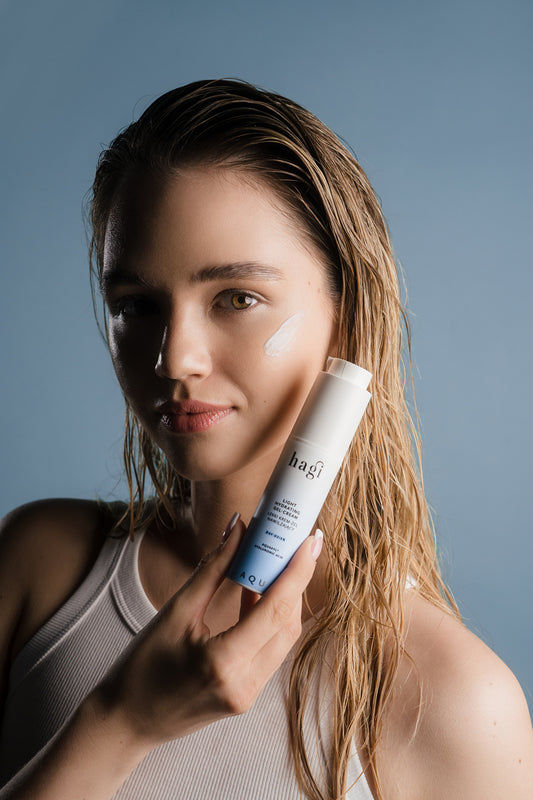 kobieta z delikatnym uśmiechem trzymająca w dłoni blisko twarzy Hagi Aqua Zone Lekki Krem-Żel Nawilżający na Dzień 50 ml